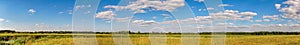 Panorama of a summer meadow against a blue sky with clouds