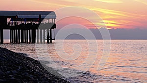 Panorama of the Sunset over the Sea next to the Silhouette of the Pier.