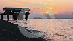 Panorama of the sunset over the sea next to the silhouette of the pier.