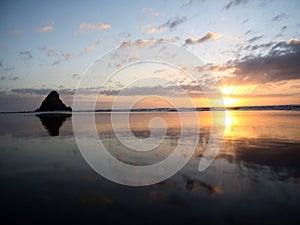 Panorama sunset reflection of Paratahi Island rock on black sand Karekare Beach West Auckland North Island New Zealand