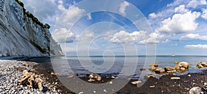 Panorama of tall white chalkstone cliffs dropping into a calm light blue ocean under a blue sky with white clouds photo