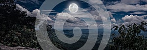 Panorama of tree and boulders against nighttime sky with cloudy.