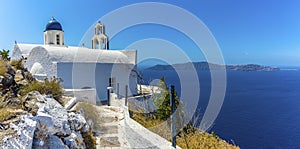 A panorama view of a blue-domed church and the distant island of Thirasia from Skaros Rock, Santorini