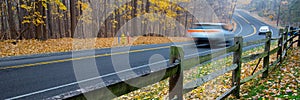Panorama view busy traffic on curved winding country road cars traffic along wooden fence, colorful fall foliage leaves carpet