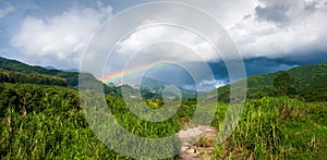 Panorama view, colorful rainbow over tropical mountain valley in the rain, scenic landscape green forest and stream in countryside