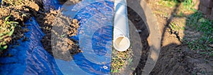 Panorama view plastic sewage pipes PVC, blue tarp with dirt, black mixing tub, pipe ready to laying, buried in ground trench,