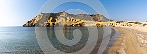 Panorama view of a secluded cove and beach on the Meiterranean coast of Spain with caves and sandstone cliffs behind