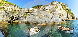 A panorama view of small fishing boats moored in front of the village of Manarola, Cinque Terre, Italy