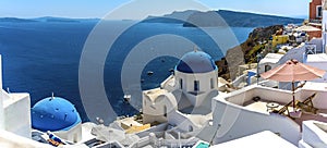 A panorama view of white painted houses and blue domed churches in the village of Oia, Santorini with Thirasia island