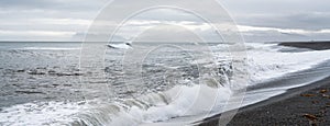 Panorama of waves crash ashore on Hvalnes beach with black lava sand on Hvalnes peninsula in southern Iceland.