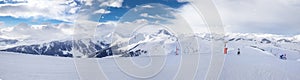 Panoramaview to ski slopes and skiers skiing in Kitzbuehel mountain ski resort with a background to Alps in Austria