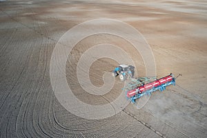 Panoramic aerial view of a field with a tractor with a trailed seeder at work.