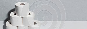 Panoramic banner with copy space, close-up of toilet paper rolls on white table, background of textured wall grey of color.