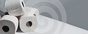Panoramic banner with copy space, close-up of toilet paper rolls on white table, background of textured wall grey of color.