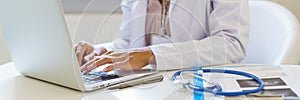 Panoramic banner with female doctor in white uniform working on laptop computer in hospital