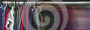 Panoramic banner. Wardrobe with clothes hanging on different colored hangers. Colorful clothes hanging on rail in wooden home