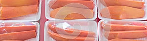 Panoramic bunch of tropical papaya slices in styrofoam trays and food film on red table in Asian market