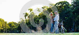 Panoramic of caucasian elderly couples standing beside a bicycle in the natural autumn sunlight garden and looking each other feel