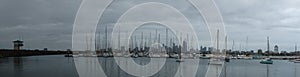 Panoramic of city of Melbourne against a sunny blue sky seen from St Kilda pier looking through the masts of yachts in the bay