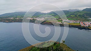 Panoramic cliff coastline town on cloudy day. Drone shot of blue water washing