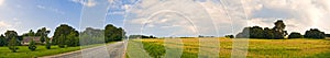 Panoramic countryside wide view of road with trees and village behind. Rural summer landscape. Typical european pastoral field