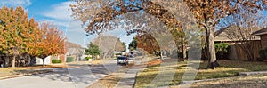 Panoramic empty sidewalk and quite neighborhood street with row of suburban house and colorful fall foliage in Texas, USA