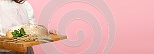 Panoramic frame. A young attractive saleswoman from a bakery shop holds a loaf of wheat flour bread and a pinch of fresh