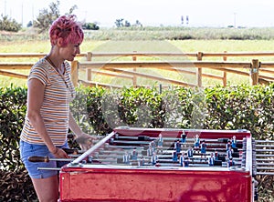 Pink short-hair woman playing table soccer (foosball) outdoors near a field photo