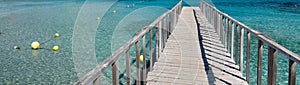 Panoramic image diminishing perspective wooden boardwalk empty path through turquoise Mediterranean Sea