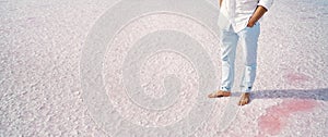 Panoramic image man legs barefoot standing on salt flats on pink salt lake, crystallized salt natural mineral formation