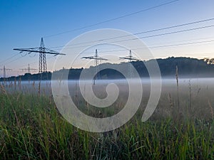 Panoramic image of a meadow with high-voltage pylons and ground fog in autumn