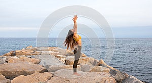 Panoramic image of young woman doing yoga on a breakwater near the sea. Urdva hastasana pose. Copy space.