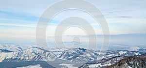 Panoramic landscape in the Altai mountains with snow-capped peaks under a blue sky with clouds in winter. White snow