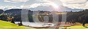 Panoramic landscape with lake aund mountainrange against sky with sun