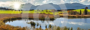 Panoramic landscape with lake aund mountainrange against sky with sun