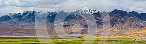 Panoramic landscape of snow-capped mountain ranges with fresh green meadows of prairie