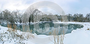 Panoramic landscape with snowy trees, calm frozen lake with reflection in water
