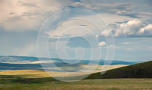 Panoramic landscape with steppe covered with green and yellow grass under blue sky with heavy clouds.