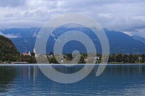 Panoramic landscape view of famous Bled Lake with colorful buildings on lake shore. Beautiful mountains in the background