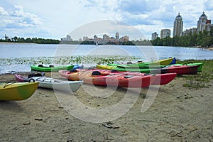 Panoramic landscape view of several colorful kayaks at the river shore. Boats on the city sandy beach, Obolon, Kyiv, Ukraine.