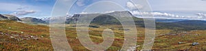 Panoramic landscape of wild nature in Sarek national park in Sweden Lapland with snow capped mountain peaks, river and lake, birch