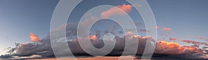 Panoramic photo of blue sky and dramatic clouds at sunset. Sunset light on the clouds.