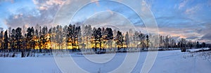 Panoramic photo of nature. Gentle sunset over the trees and the snow-covered river. Beautiful clouds illuminated by the evening su