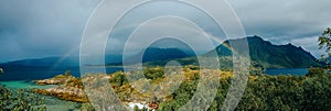 Panoramic photo of rainbow, sea, hills, blue sky in Norway on summer.