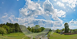 Panoramic photo of the river near the forest under the blue cloudy sky