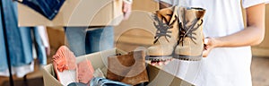 Panoramic shot of african american volunteer holding kids shoes while standing near carton box with footwear.