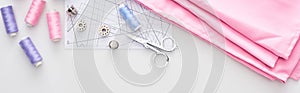 Panoramic shot of fabric, sewing pattern, scissors, thimbles, bobbins and threads on white background.