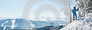 Panoramic shot of a female skier resting on top of the mountain observing nature at ski resort