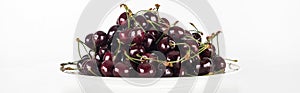 Panoramic shot of fresh, sweet, red and ripe cherries on white plate.