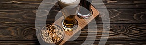 Panoramic shot of glasses of dark and light beer near bowl with roasted peanuts on wooden table.